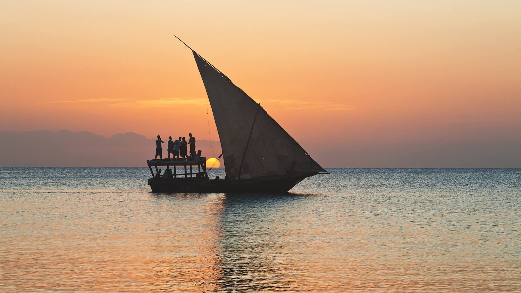Eine traditionelle Dhow auf dem Indischen Ozean vor der Küste Kenias, dahinter eine palmengesäumte Küste
